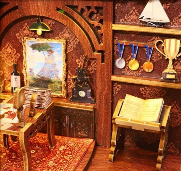 A beautifully detailed DIY book nook kit featuring a vintage study scene. The miniature setting includes an ornate wooden desk with stacked papers, a bookshelf displaying medals and a trophy, an open book on a stand, and a framed painting on the wall. The warm lighting and intricate design create a cozy and elegant atmosphere.