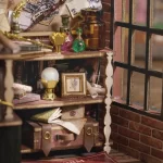 A close - up of a detailed DIY miniature shelf inside a magic wand shop, featuring potions, scrolls, a framed picture, and a trunk.