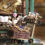 A close - up of a miniature cart in a DIY magic wand shop, loaded with books, a golden wand, glass orbs, and a suitcase.