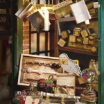 Close - up of a section in a DIY magic wand shop miniature, showing hanging books, wands, an owl figurine, and a globe filled with colorful items.
