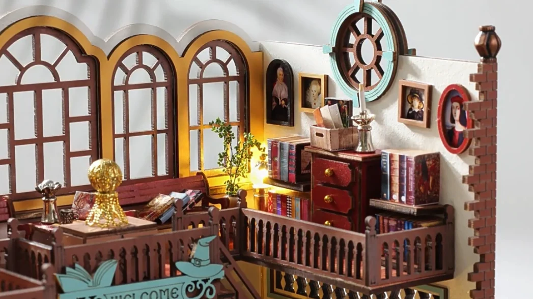 A detailed view of the upper level of a DIY magic book store miniature house, featuring arched windows, bookshelves, framed pictures on the wall, and decorative elements.