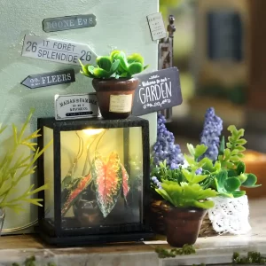 Close-up of miniature plants, a "Welcome to our GARDEN" sign, and other decorative elements outside the plant dollhouse.