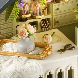 Close-up of a miniature desk with pink roses in a vase, a golden frame, and scissors inside the plant dollhouse.