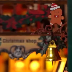 Close-up of a miniature gingerbread man with a Santa hat above a golden bell in the Christmas Shop DIY Book Nook Kit.