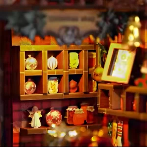 Close-up of miniature shelves in the Christmas Shop DIY Book Nook Kit, filled with tiny jars, ornaments, and an angel figurine, with a golden bell in the foreground.