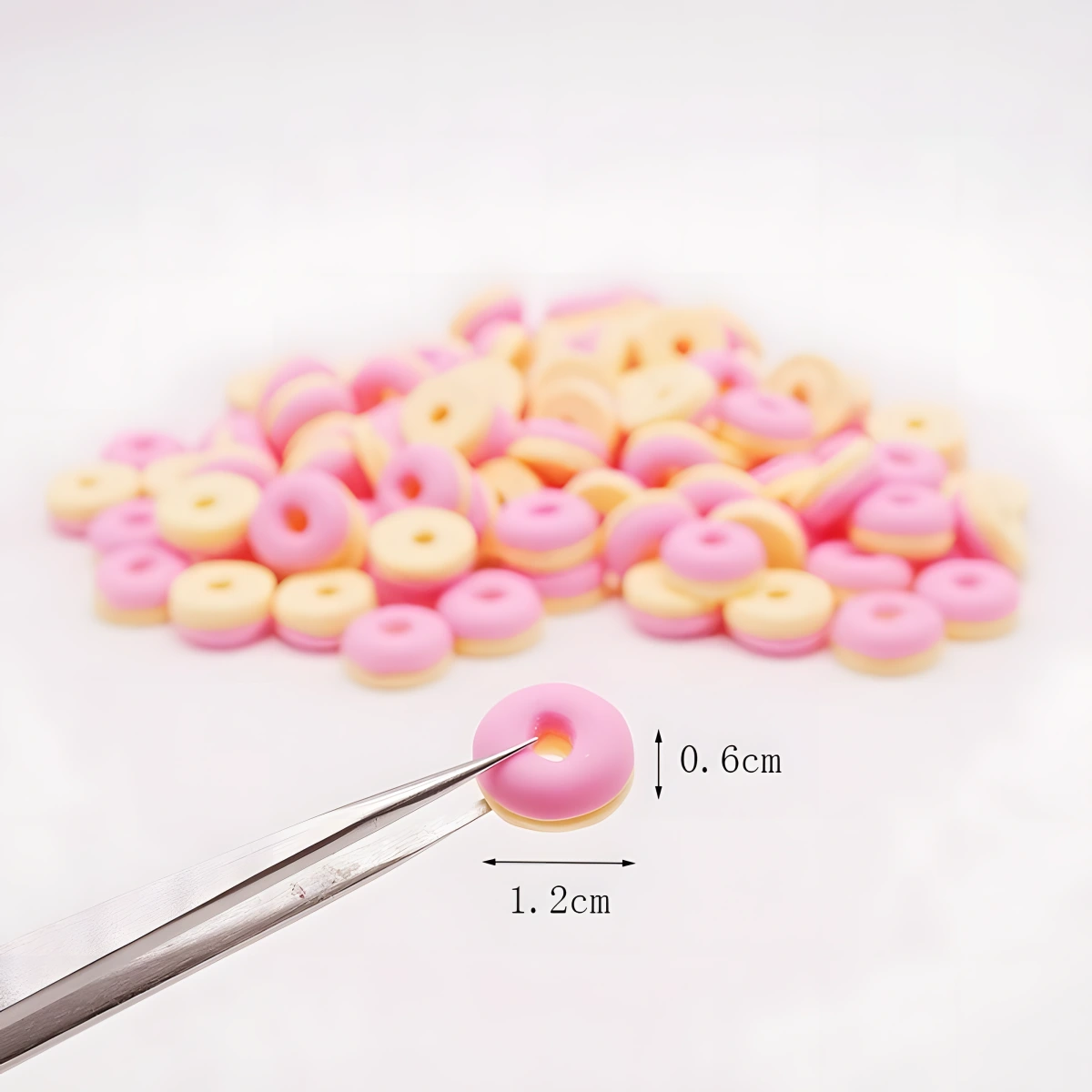 A tiny pink miniature donut held by tweezers, showing its size.