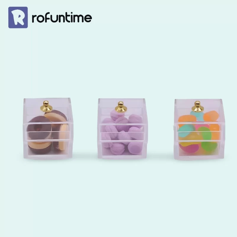 Three small, clear plastic boxes, each filled with miniature sweets, including donuts, macarons, and colorful gummy candy beads.
