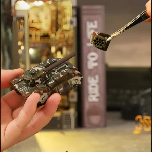 Hands assembling the Military Base DIY Book Nook Kit, showing a miniature tank and tweezers placing a small component.
