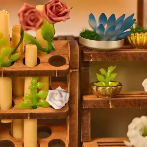 Detailed close-up of miniature flower and plant arrangements on wooden shelves, including small pink roses, green foliage, a blue succulent, and white flowers, inside the Bloomsomary Atelier.