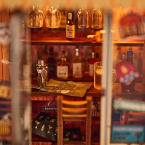 A detailed interior shot of a miniature bar, showing hanging glasses, liquor bottles, a cocktail shaker, a menu, and a bar stool.