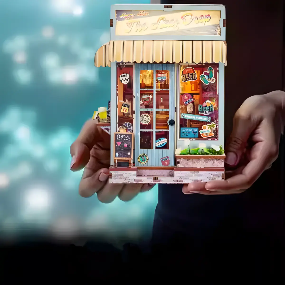A pair of hands holding the miniature beach bar book nook kit, with a blurred background.