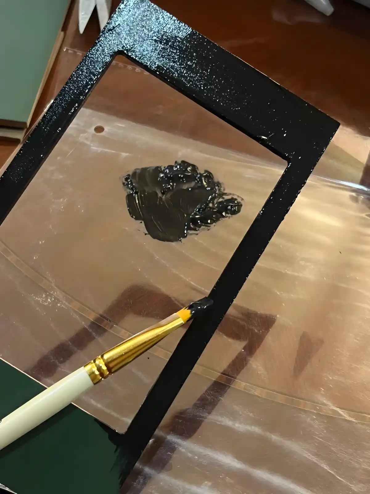 A hand painting a tiny black picture frame, an essential part of the Rofuntime DIY miniature house makeover kit.