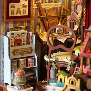 Close-up of the miniature workshop, showing a chair, a bookshelf with tiny books, a glue bottle, rulers, and various small craft supplies.