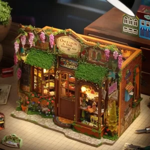 A top-down, angled view of the finished dollhouse on a craft table with rulers, tools, and another tiny dollhouse, suggesting a DIY project.