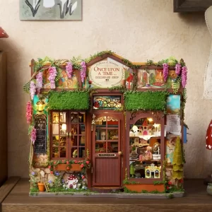 A straight-on view of the miniature dollhouse storefront, featuring a detailed door, a stained-glass window, overgrown vines with pink flowers, and a blackboard sign on the left.