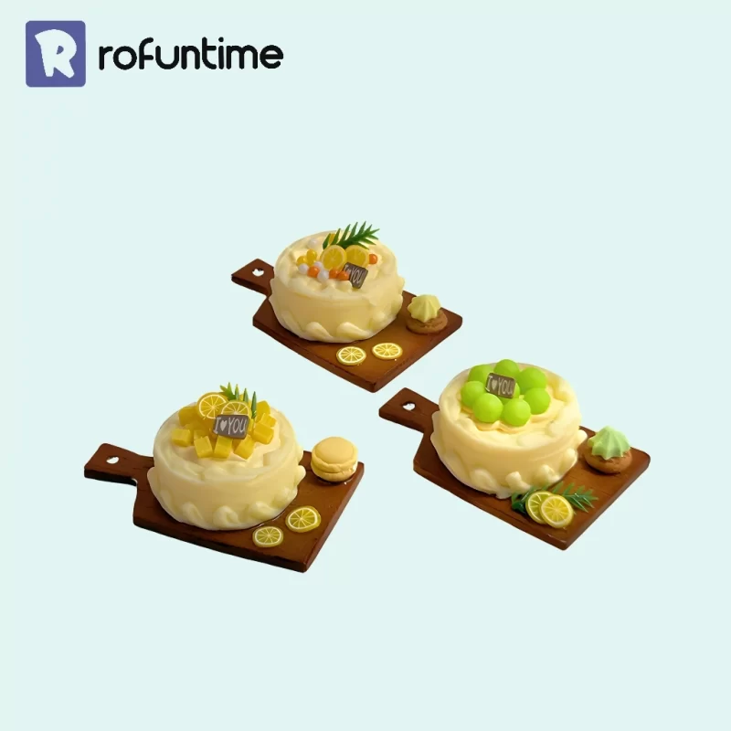 Three miniature cakes on wooden cutting boards. One cake has green grapes, one has yellow fruit cubes, and one has citrus slices. The Rofuntime logo is in the top left corner, and the background is light blue.