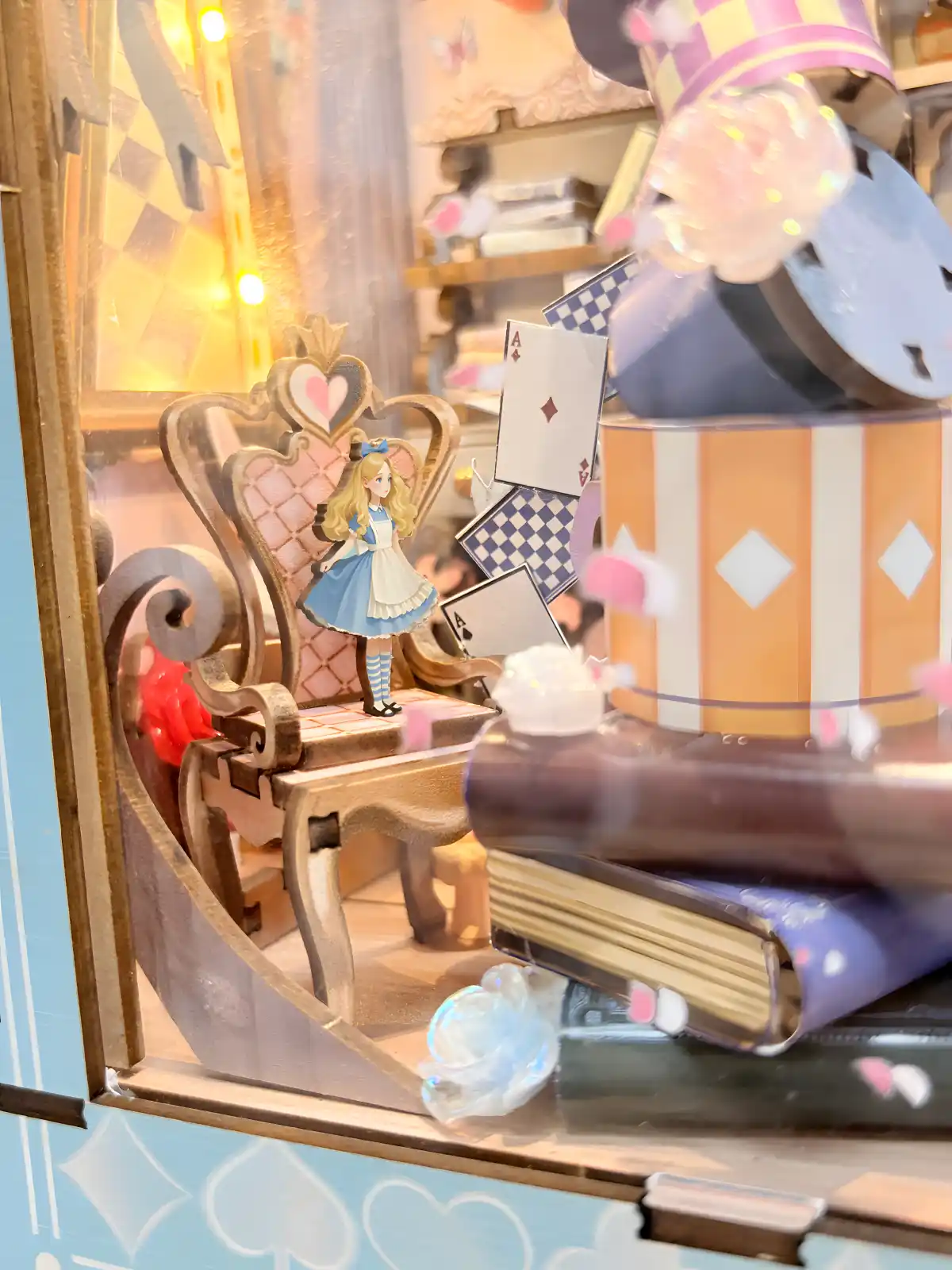 A miniature Alice figure standing on a chair inside a beautifully lit fairy tale book nook kit.