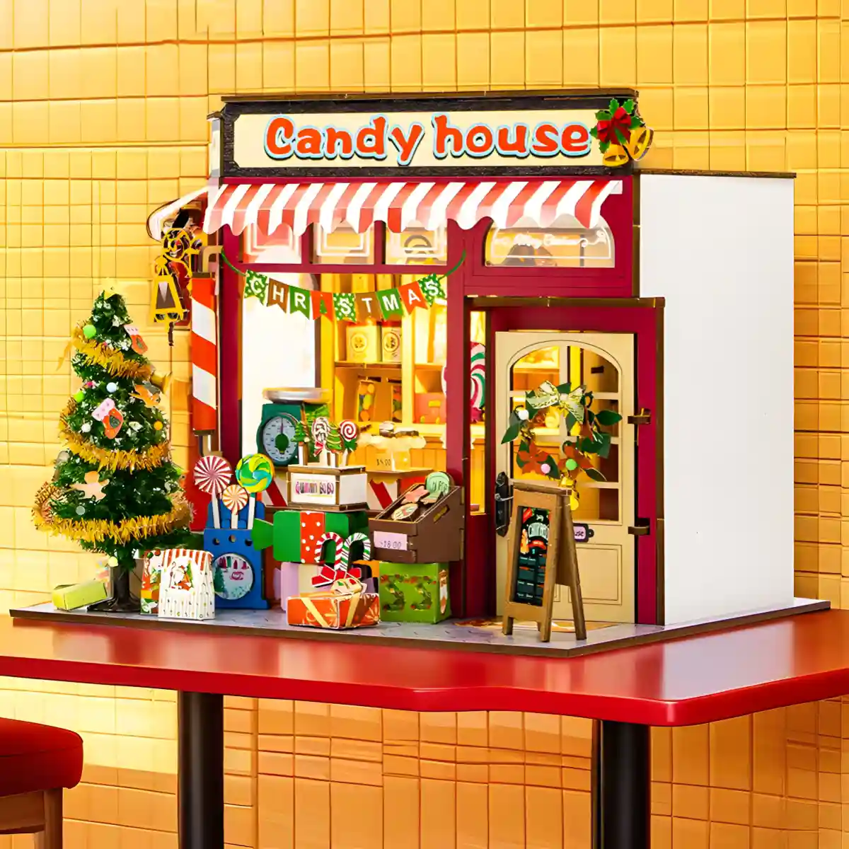 Side-angle view of the festive miniature house, fully assembled and lit, on a red table.