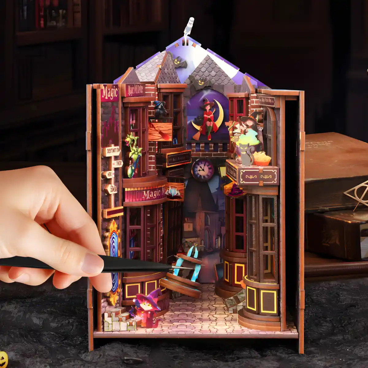 Assembling the Magic Alley book nook with tweezers, carefully placing details inside the fantasy world structure with its many wizard shops.