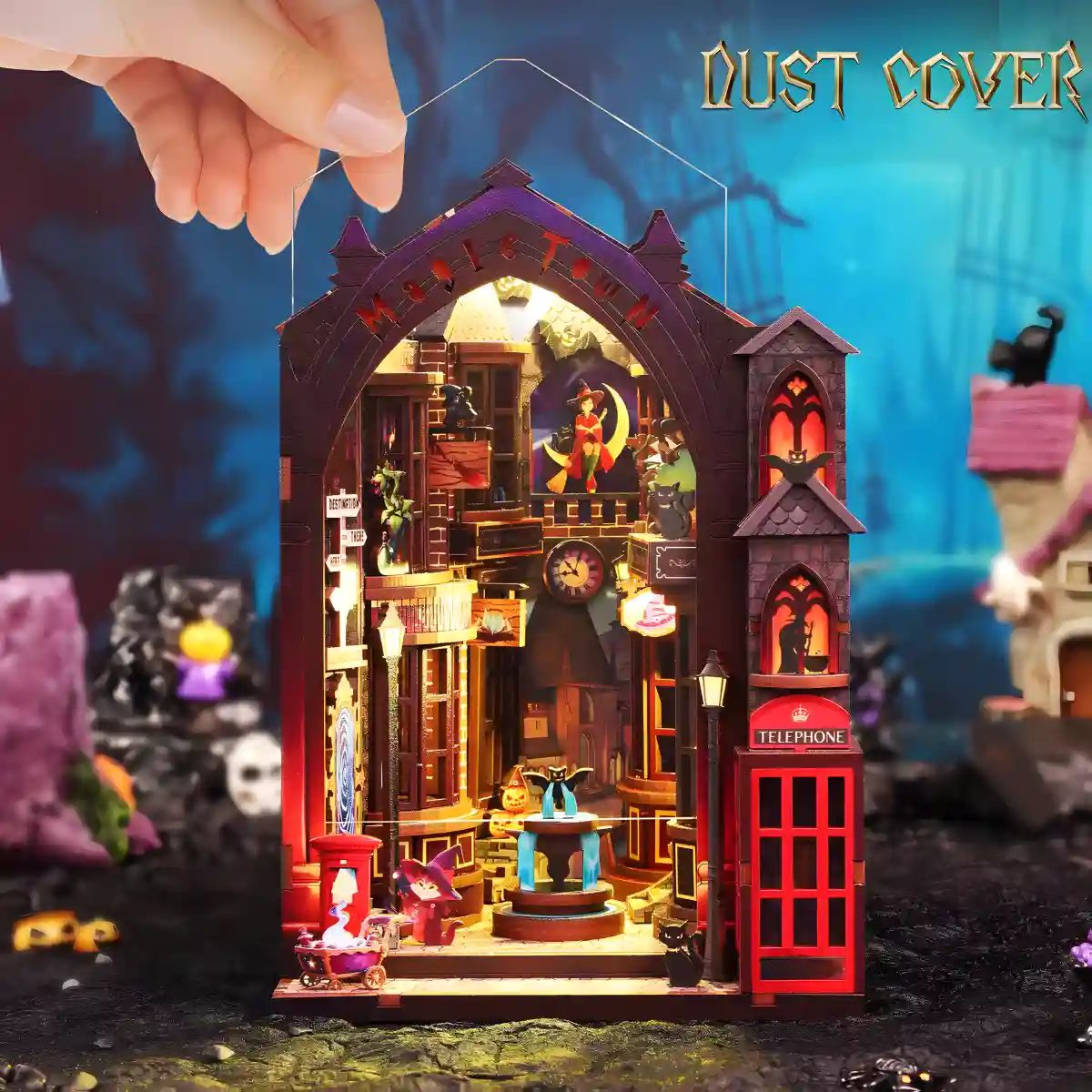 A hand placing a clear dust cover over the Magic Alley book nook, protecting the magical fantasy world scene and its gothic details.
