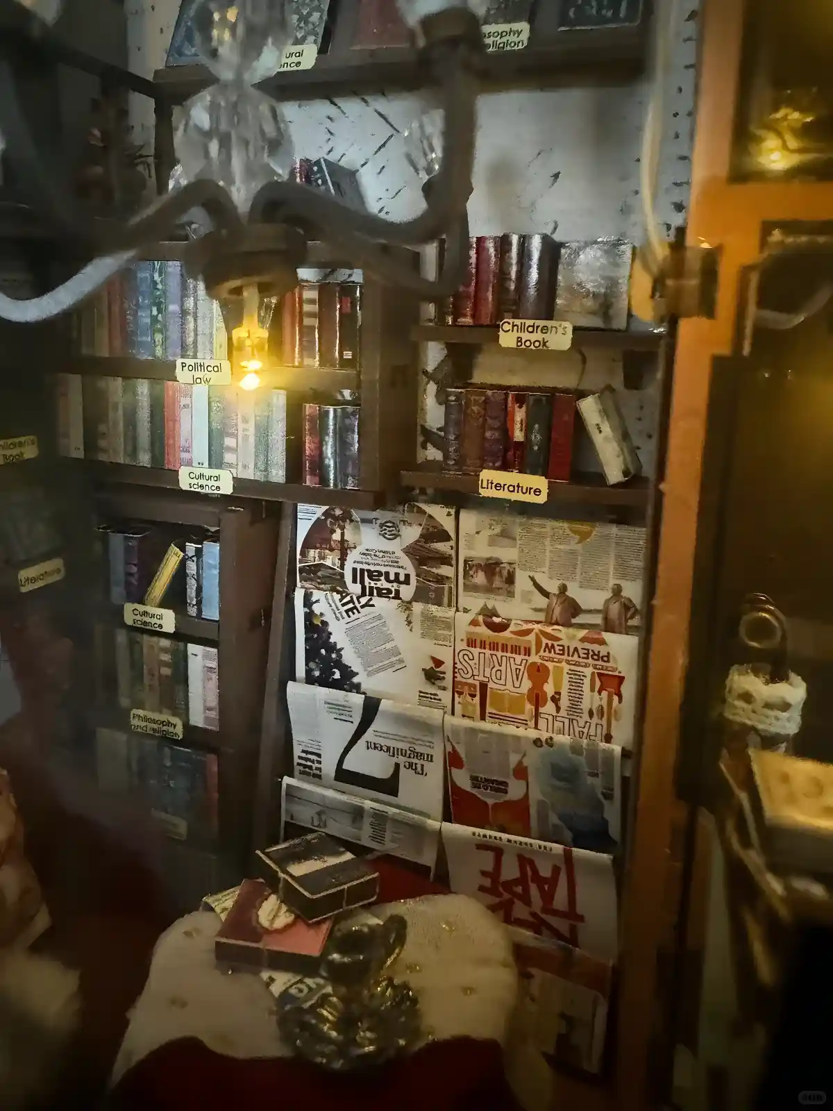 Interior of a Soul Bookstore book nook makeover, detailing miniature bookshelves, a magazine rack, and warm chandelier lighting.