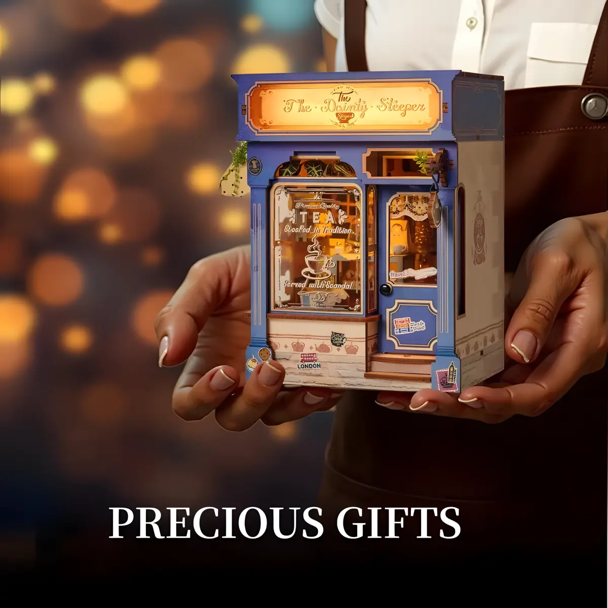 The Dainty Steeper book nook kit, miniature English vintage tea shop held in hands, glowing light.