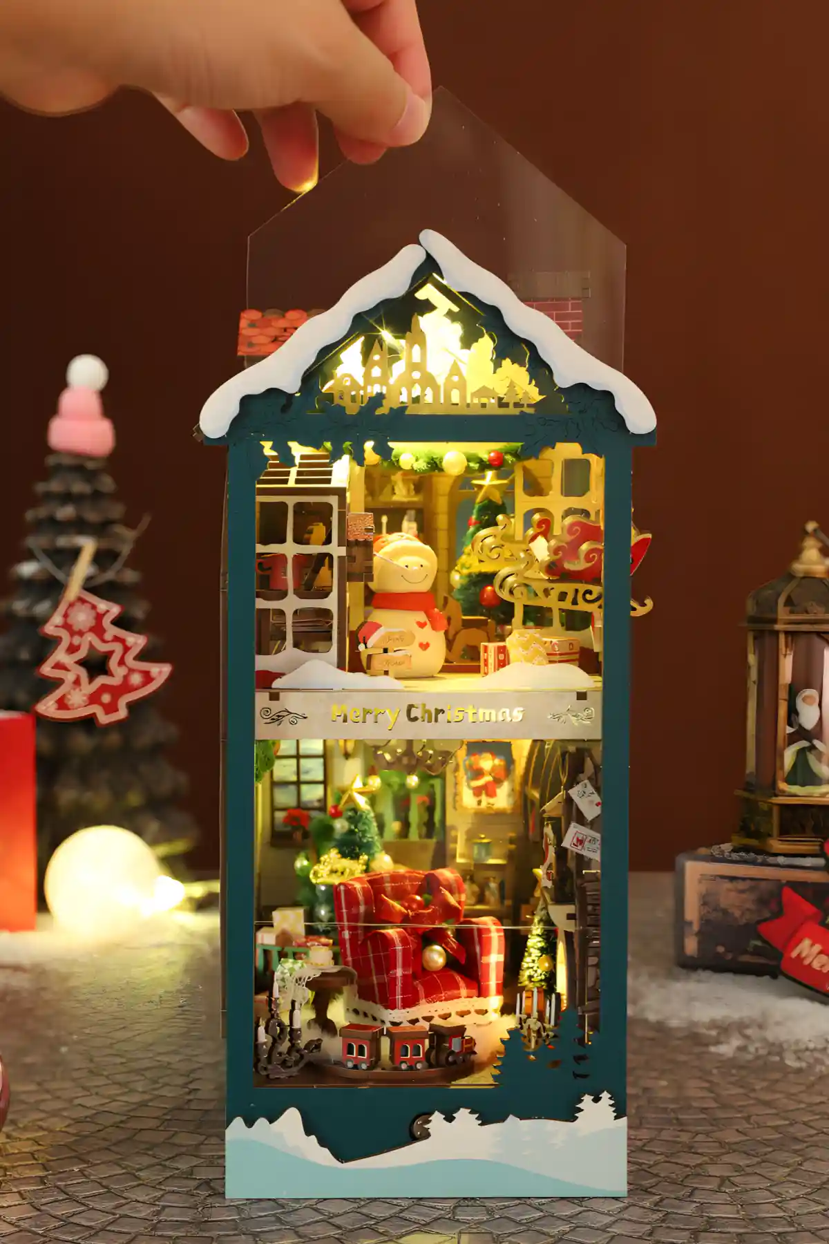 Illuminated Merry Christmas book nook with a snowman figure, red armchair, and dust cover.