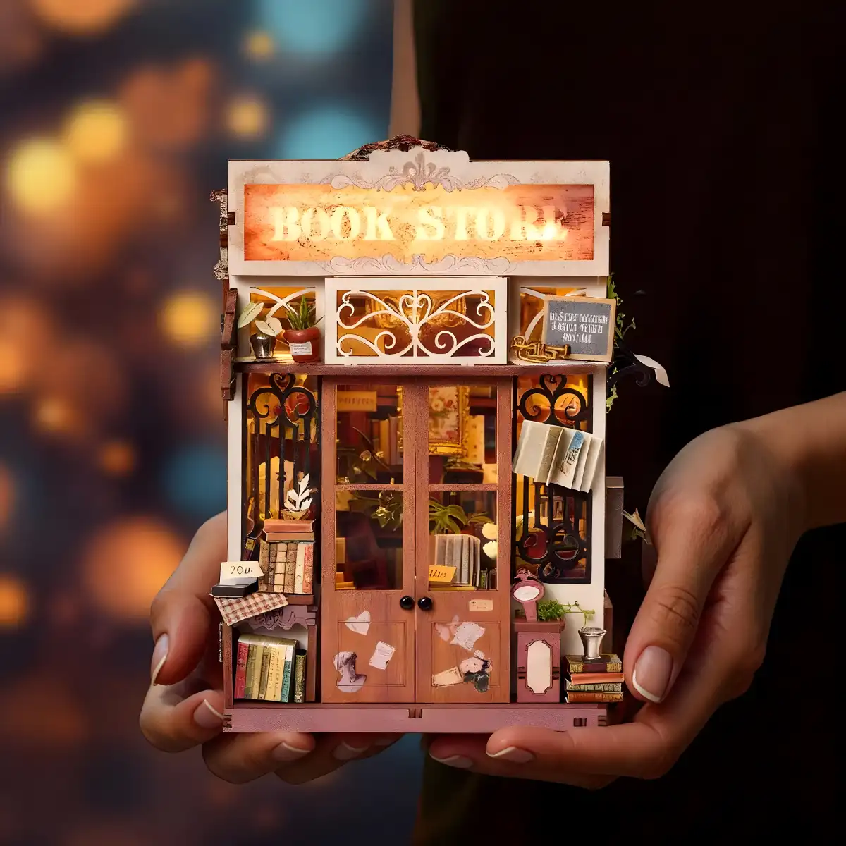 Assembled and lit Art Bookstore DIY Book Nook Kit held in hands, showcasing its compact display size.