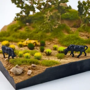 Realistic model landscaping grass application on a miniature diorama base with rocks and figures.