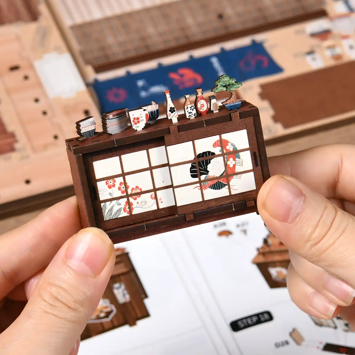 Close up of hand-holding miniature Japanese cabinet with paper doors and bonsai