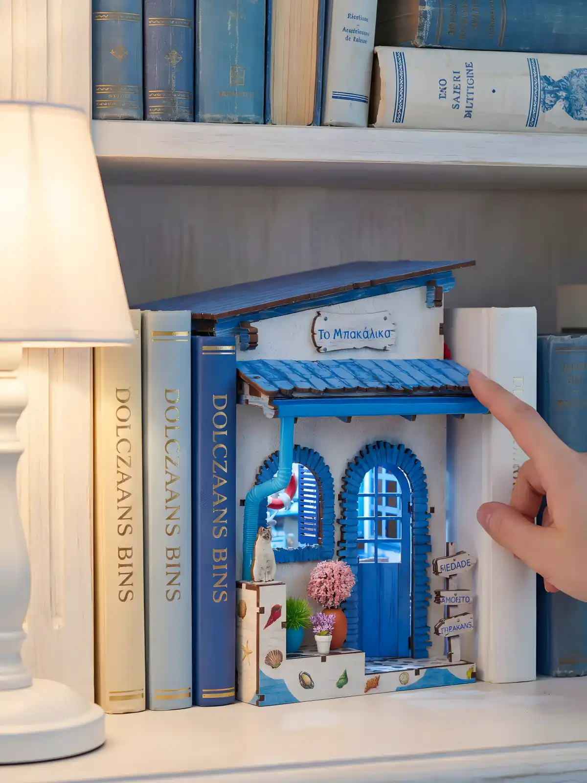 Greek island miniature house tucked between blue books, perfect as coastal bookshelf decor.