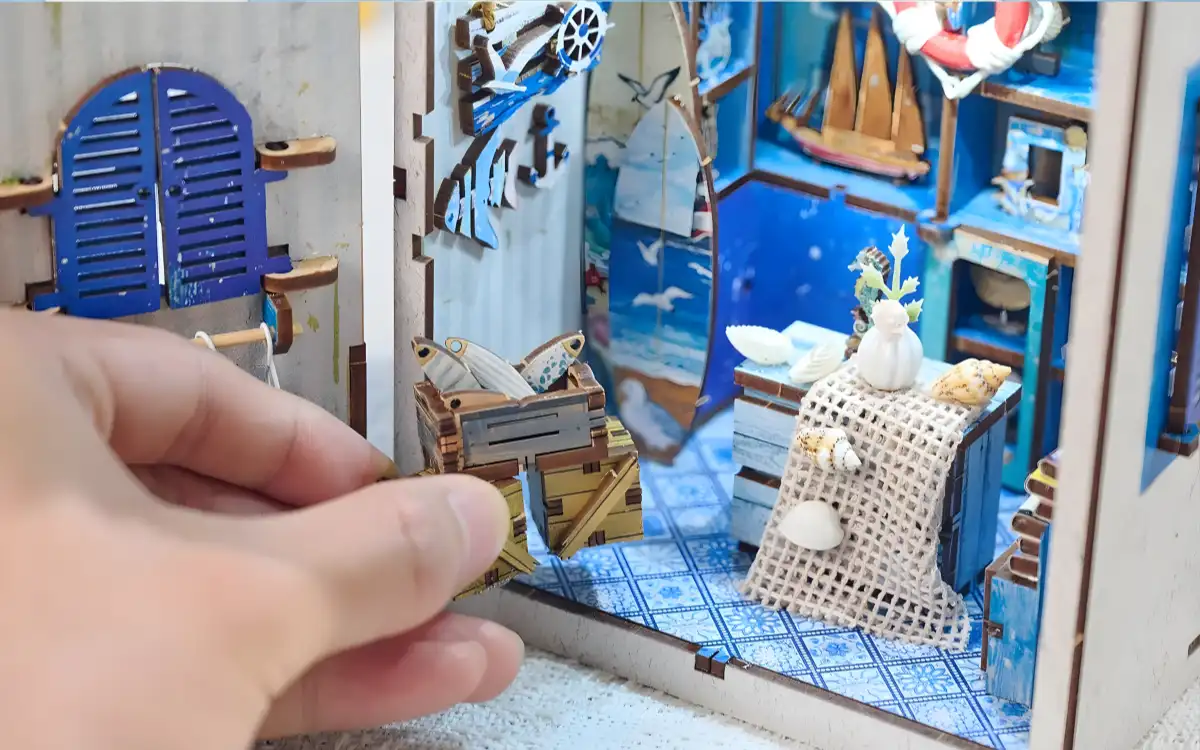 Hand placing a tiny wooden fish crate inside an immersive DIY book nook shop.