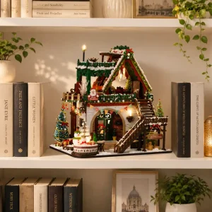 Glowing winter cabin miniature illuminated on a bookshelf alongside books for cozy festive home decor.