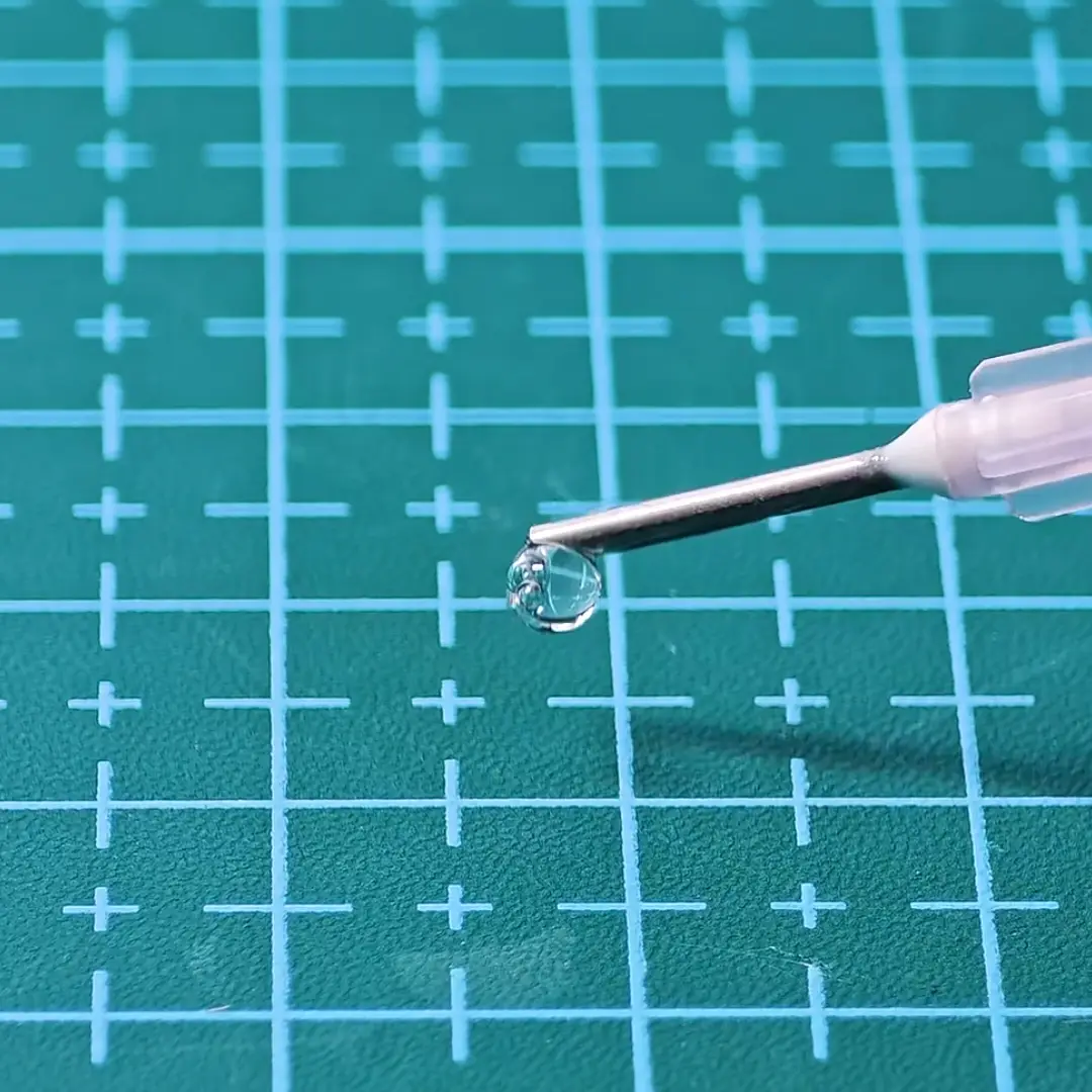 Precision glue applicator for miniatures showing clear liquid droplet on fine needle tip