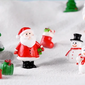 Miniature Santa Claus standing with twin snowmen and green gift boxes on snow